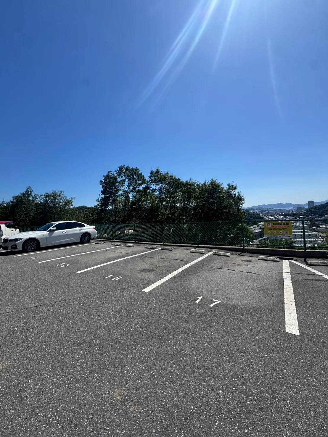 牛田早稲田の施工後の全景。別の角度から、フェンス沿いの駐車区画、周囲に残る木々、遠くの街並みを見た状態。