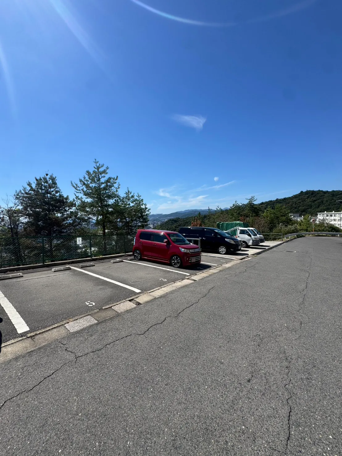 牛田早稲田の伐採後。奥の駐車区画の周囲で木々の重なりが減り、フェンス越しに残る木の幹や枝が見える。