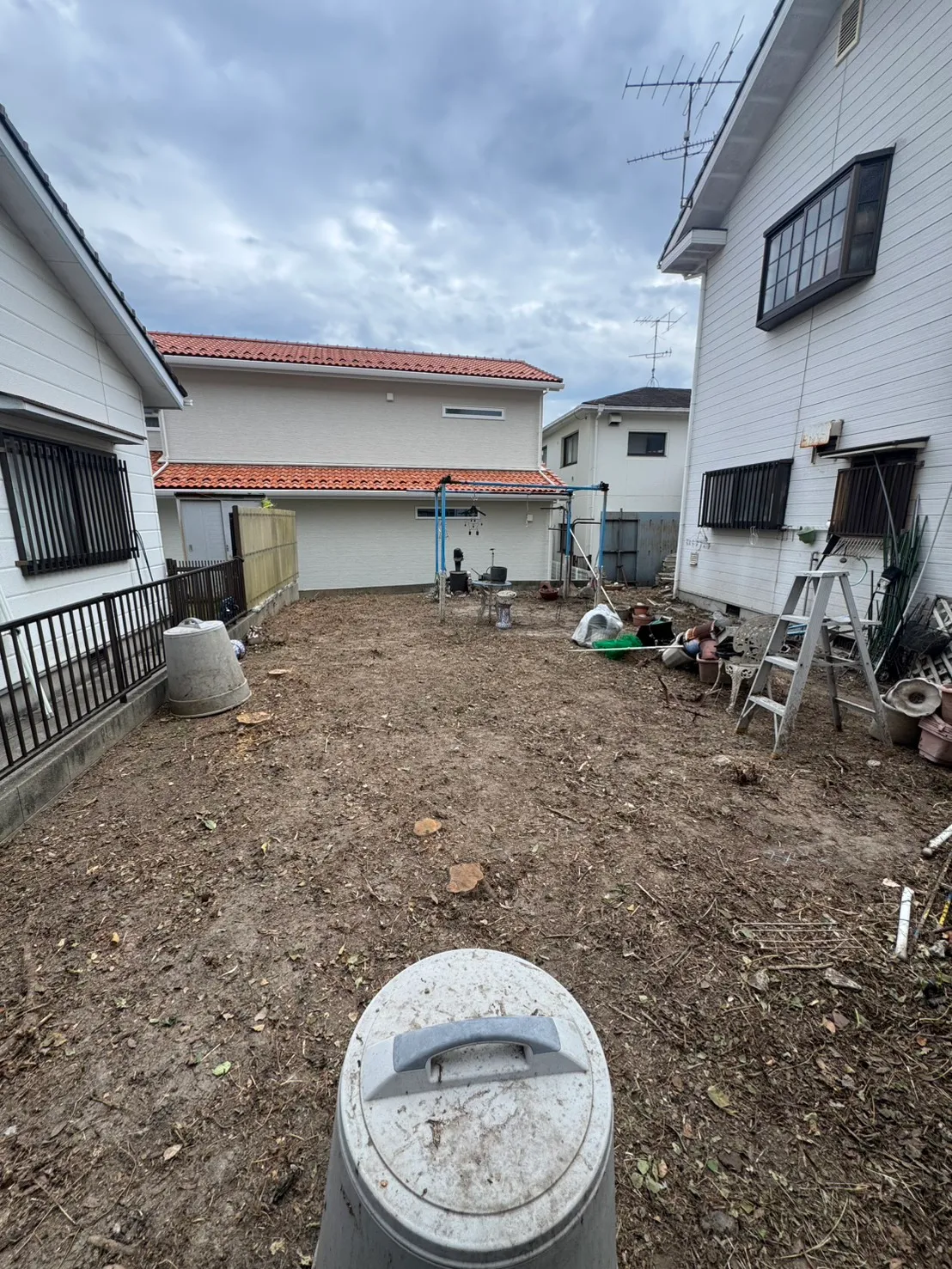 住宅に囲まれた伐採・草刈り後の庭と、地面に残る切り株